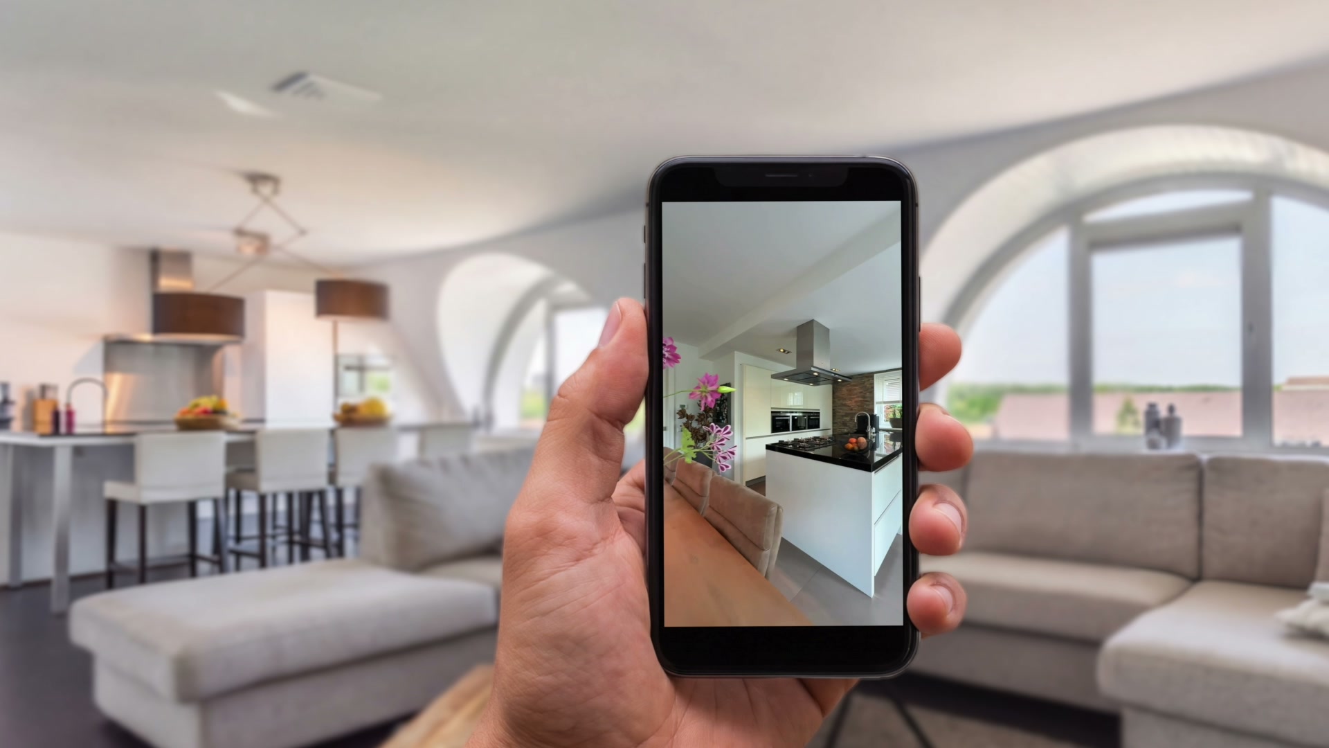 Een hand met een telefoon waarop woningreels te zien zijn, met een interieur op de achtergrond